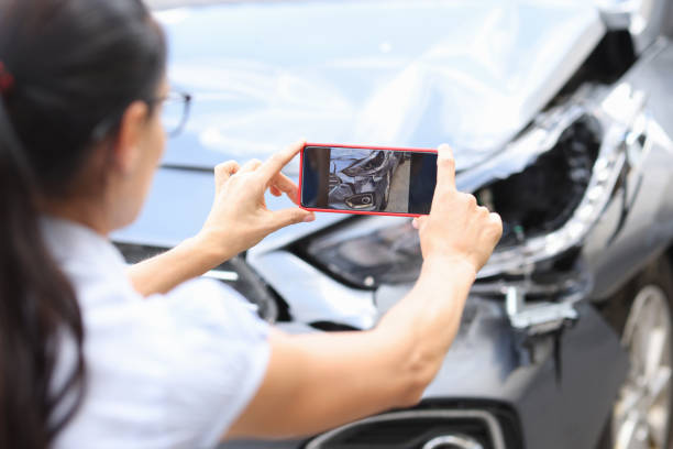 A woman takes a photo of her broken headlight after a car crash.