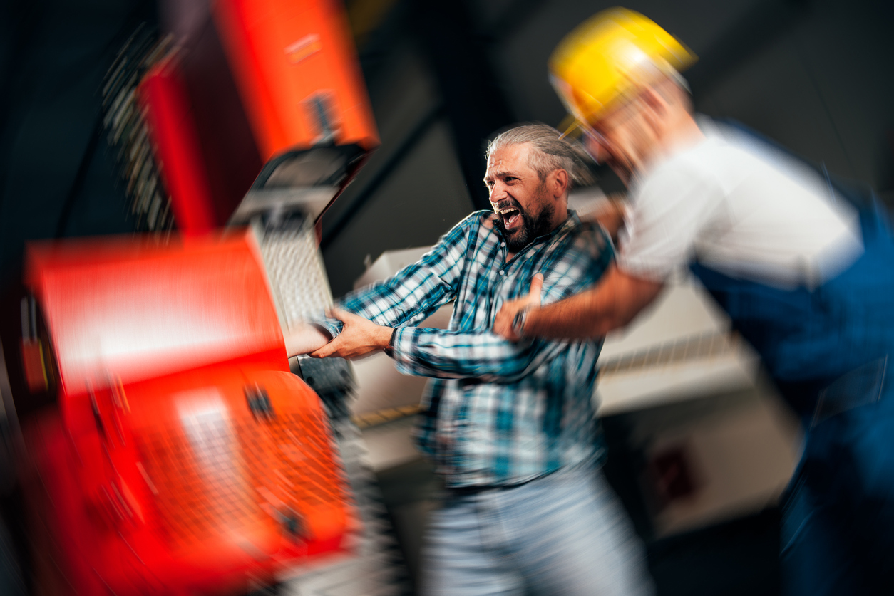 A worker whose hand has been caught in a piece of machinery being helped by another worker.
